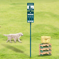 Green outdoor dog waste station with bin, bag dispenser and reflective sign on a metal pole